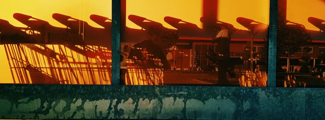 A shopfront window at dusk, its glass thrown so orange by the low sun that the store behind it has disappeared and only the street outside is reflected back.