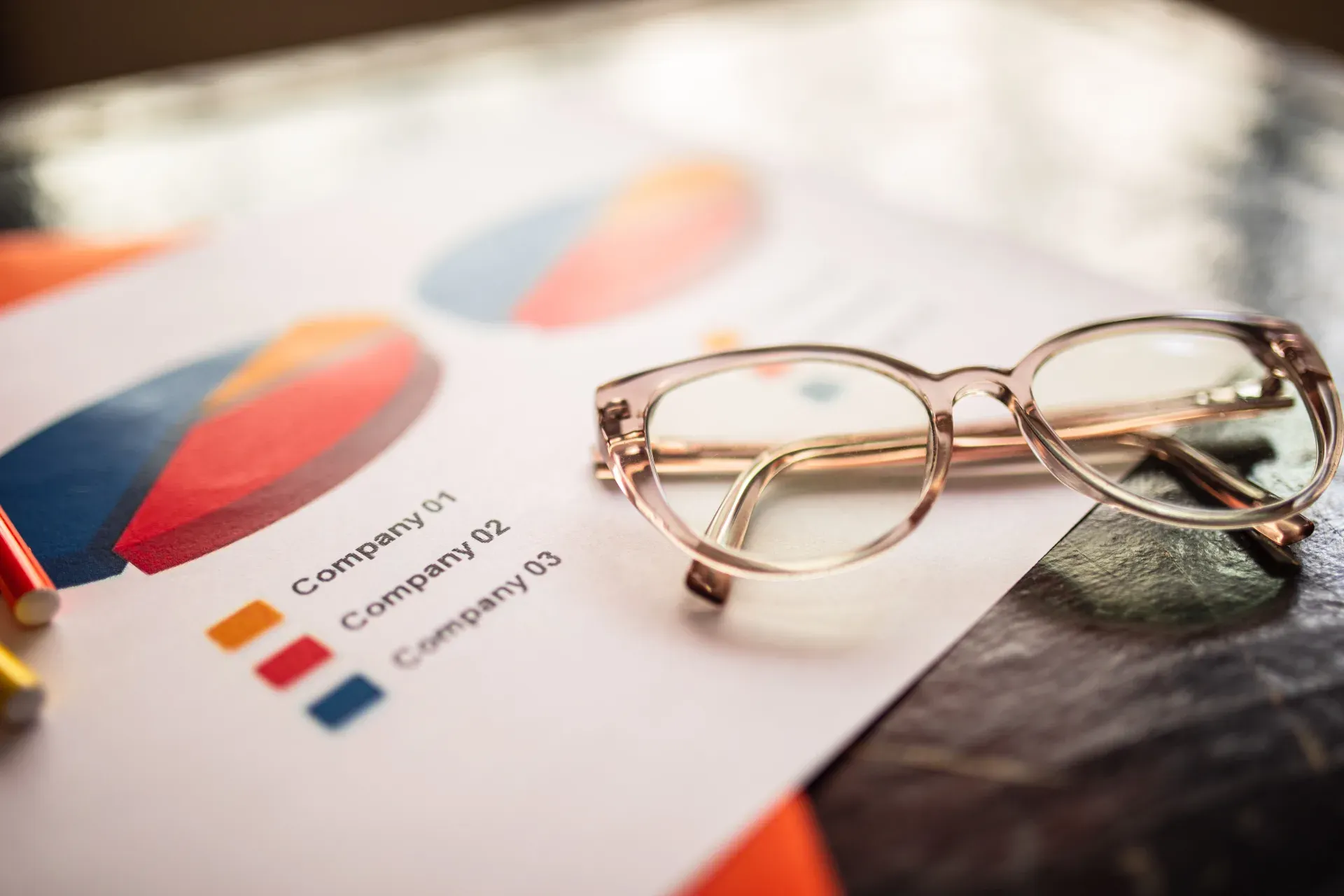 Reading glasses resting on a printed company-comparison pie chart