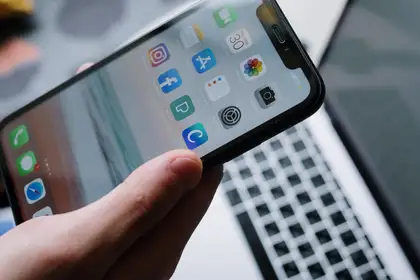 A phone held in one hand over an open laptop, both screens lit — the two surfaces an audit covers.