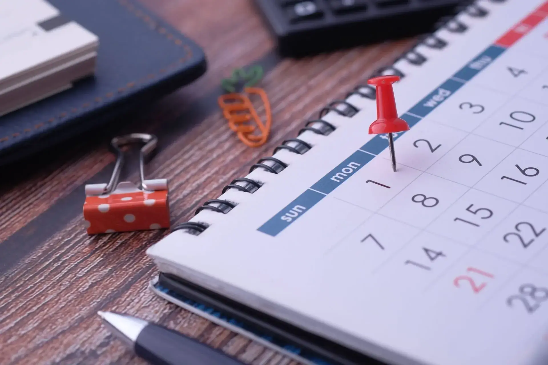 A red pin pushed into a single date on a spiral desk calendar.
