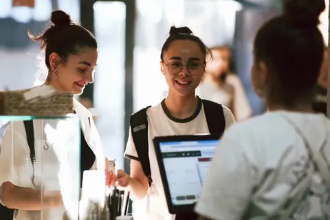 Two shop assistants at a counter taking a customer through a checkout on a point-of-sale tablet.