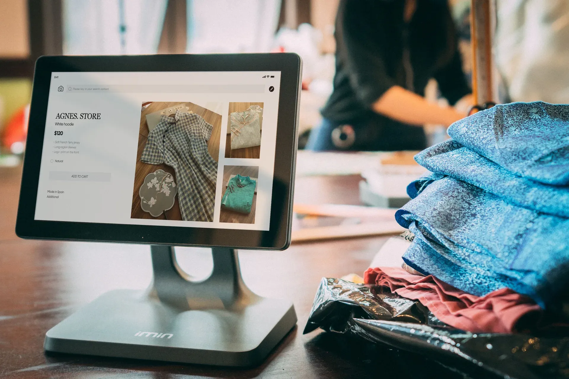 A tablet POS displaying a storefront product page beside folded fabric stock on a countertop