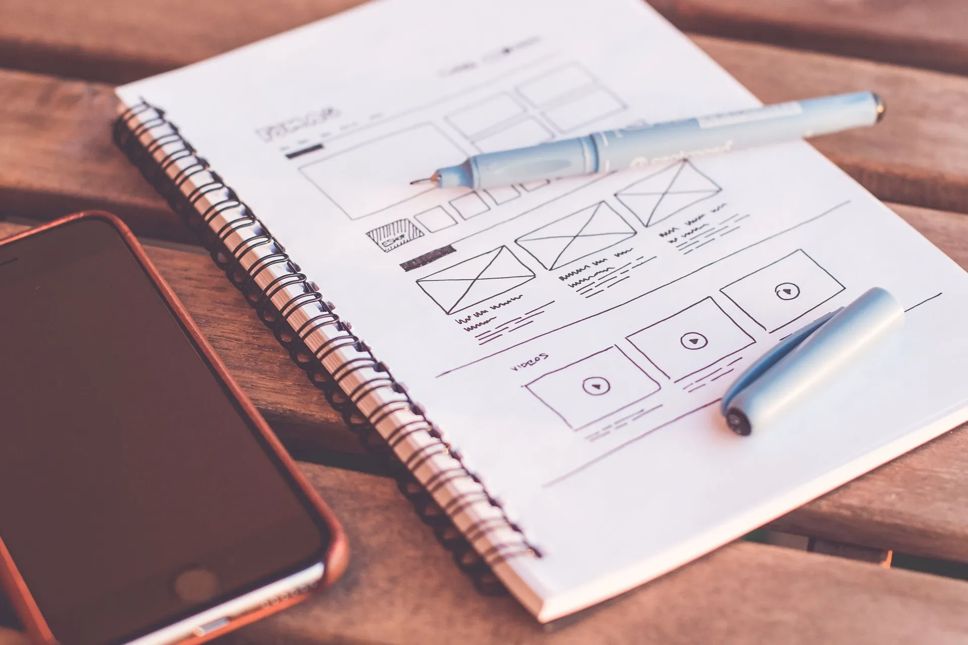 Hand-drawn website wireframes in an open sketchbook beside a laptop, the layout of several pages visible at once